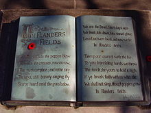 A sculpture in the form of an open book. The text of the poem "In Flanders Fields" is written within and a small red poppy lays on top.